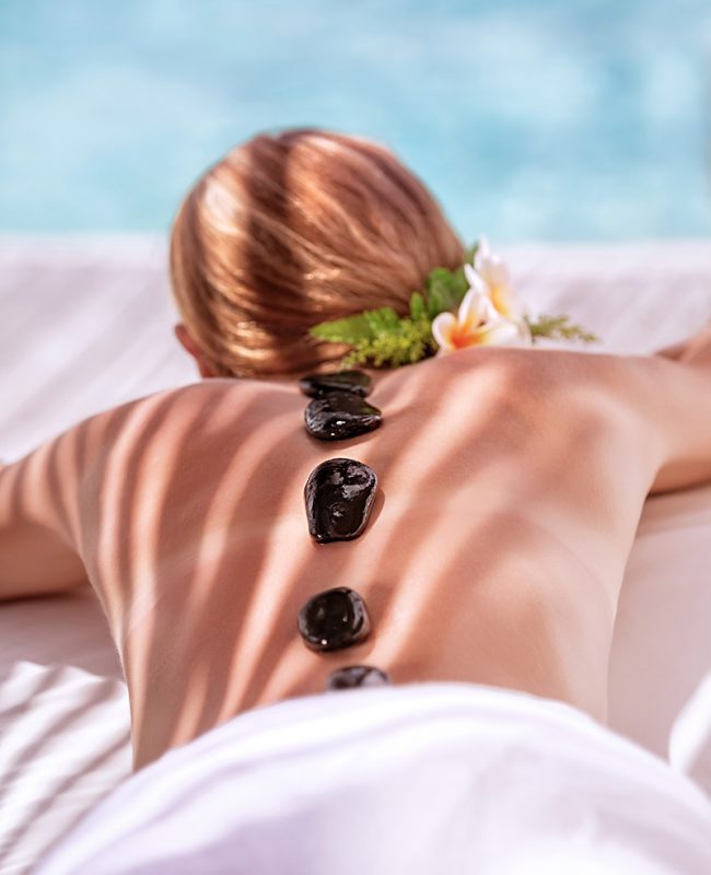 Hot stone massage on luxury spa resort on the beach, young beautiful woman lying down outdoors and enjoying dayspa, summer vacation concept